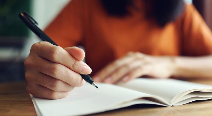 A young woman writes in an empty notebook.