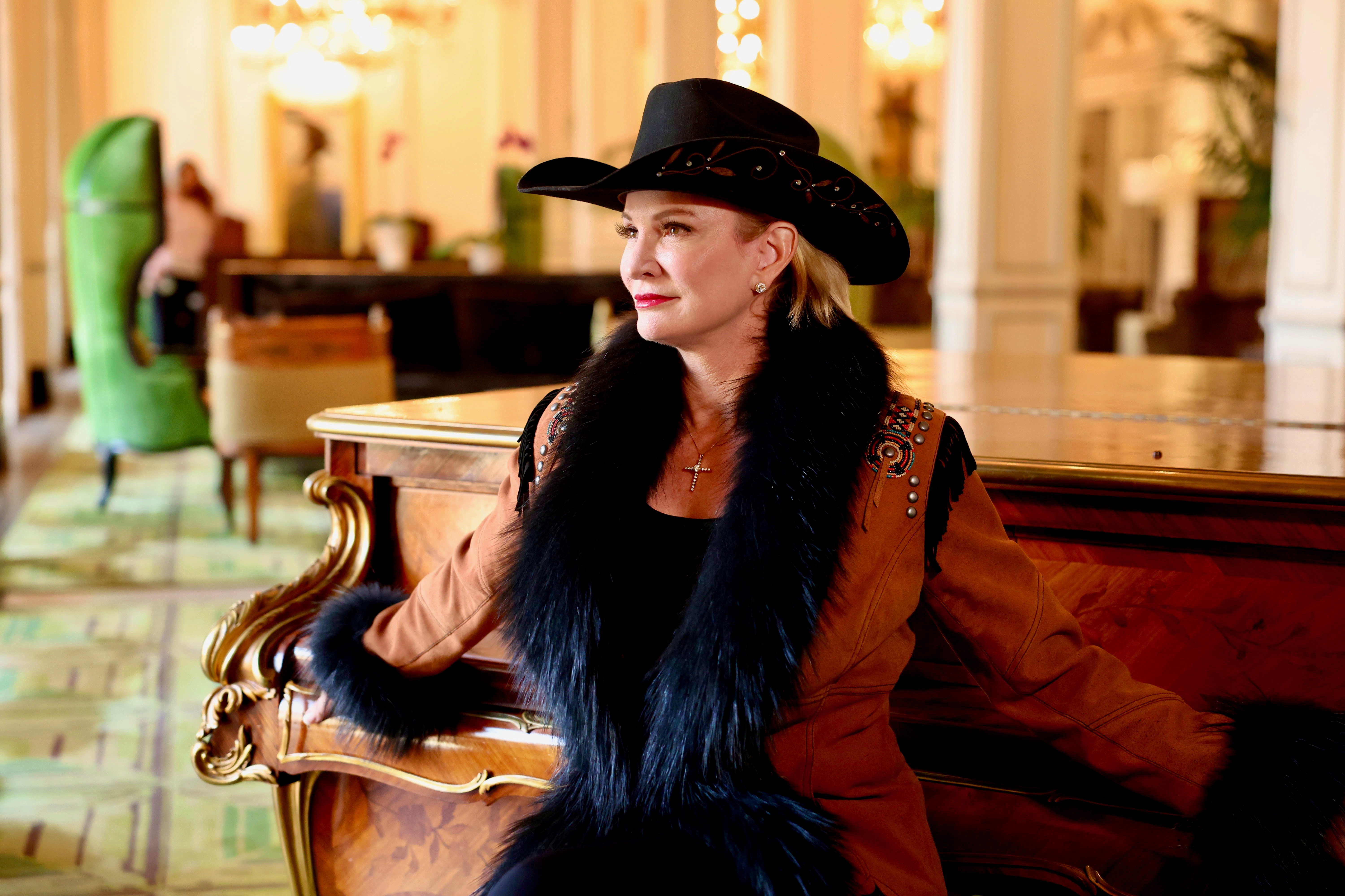 Commissioner Dawn Buckingham, M.D. sitting at a piano wearing a cowboy hat and fur-fringed coat