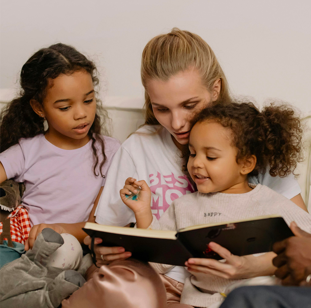 A mom and her two daughters read a book on the couch.