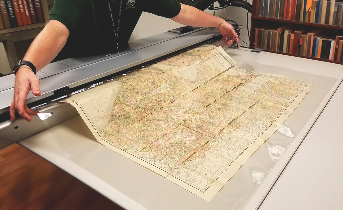 A scan lab employee feeding a original map through a large image scanner