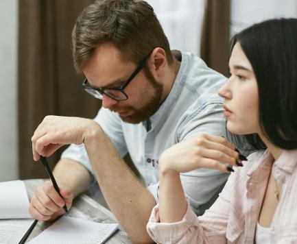 A man with glasses and a woman take notes and listen in class