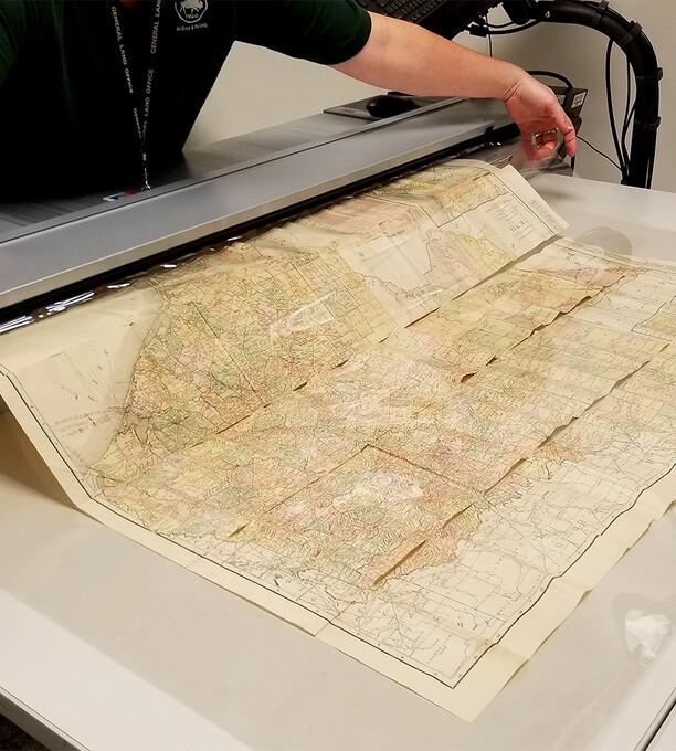 A scan lab employee feeding a original map through a large image scanner.