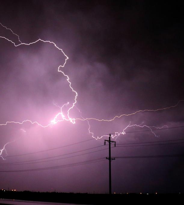 Lightning in a dark sky behind a power line. 